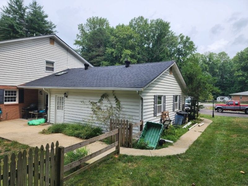 Exterior view of a white siding house with a dark shingle roof, a patio, a wooden fence, and a green yard.