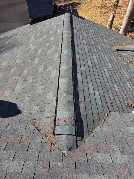 High-angle shot of a shingled roof featuring a hip ridge vent with worn, multi-colored asphalt shingles.