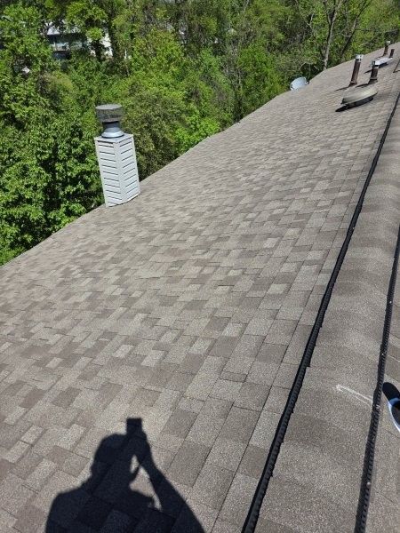 A view from above looking down a shingled roof towards a chimney, with a person’s shadow visible in the foreground.
