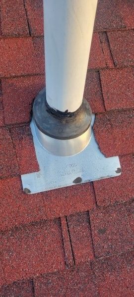 A white plumbing vent pipe emerging through a metal flashing base installed on a red asphalt shingle roof.