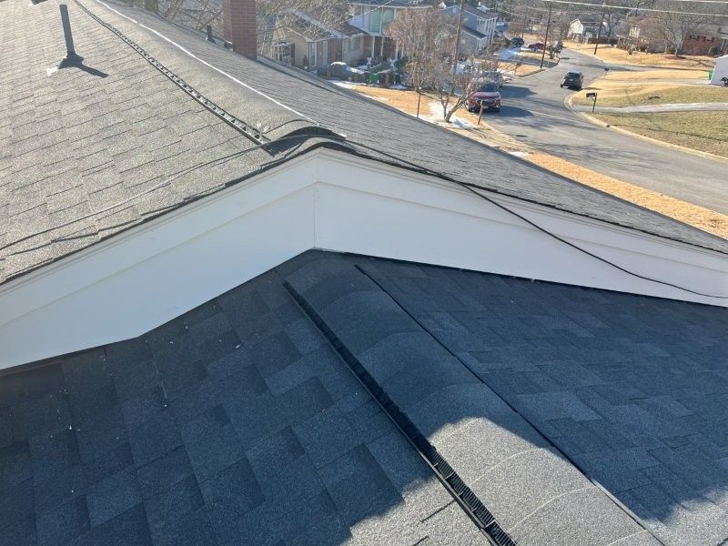 A view from a rooftop looking down at a gable roof intersection with white trim and grey shingles, overlooking a street.