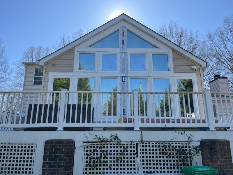 A tan house with large, reflective windows, a white deck railing, and a lattice base beneath a bright, sunny sky.