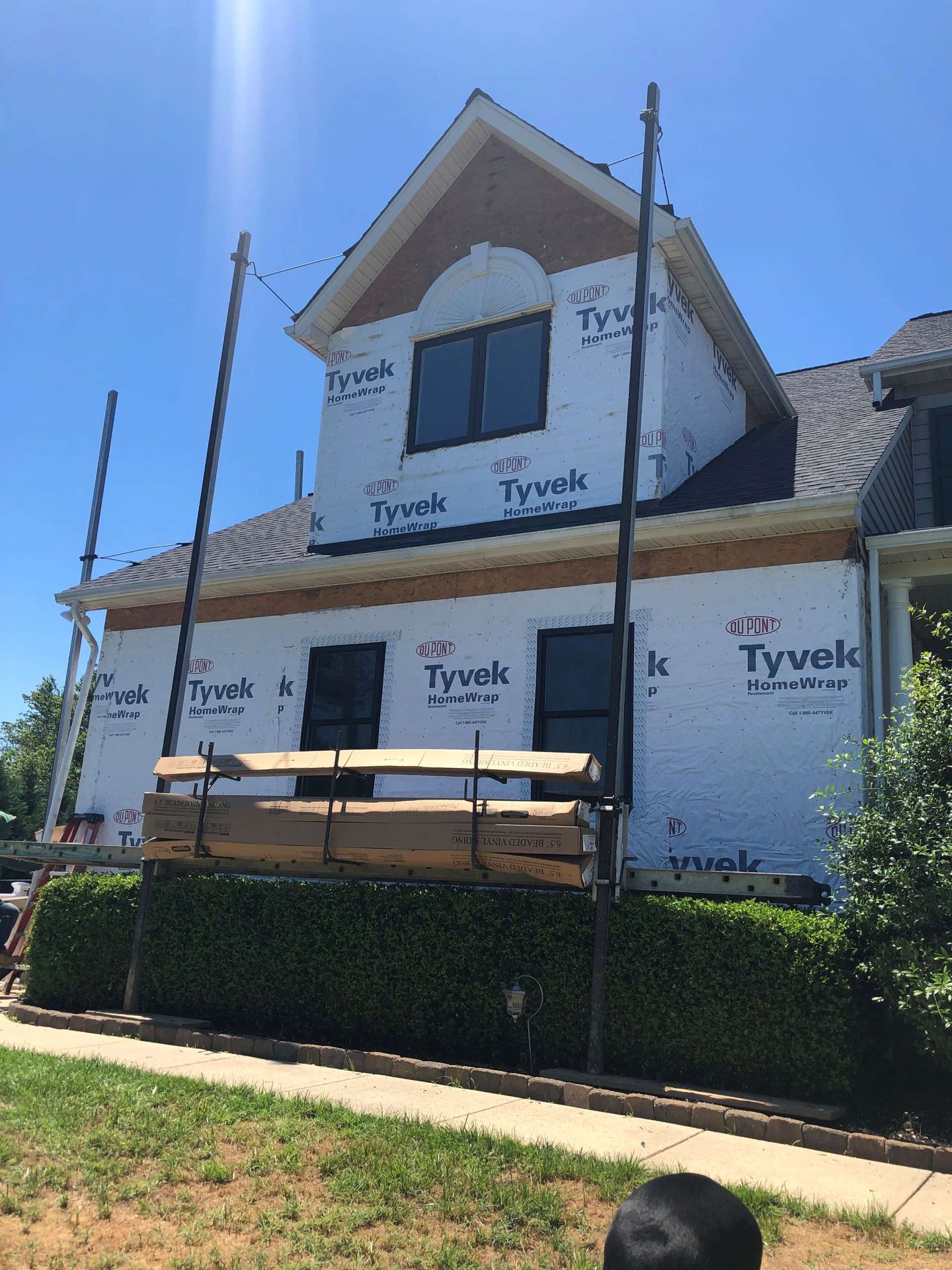 A residential home under construction, covered in white Tyvek wrap with scaffolding set up in front of the lower level.